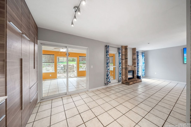 unfurnished living room featuring rail lighting, light tile patterned flooring, a fireplace, and ceiling fan