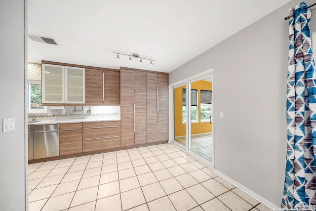 kitchen with light tile patterned floors, light countertops, visible vents, stainless steel dishwasher, and glass insert cabinets