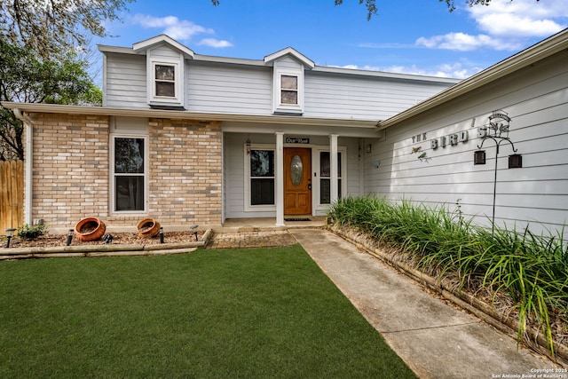 view of exterior entry featuring brick siding, a lawn, a porch, and fence