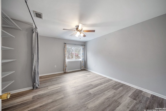 unfurnished room with ceiling fan, wood finished floors, visible vents, and baseboards