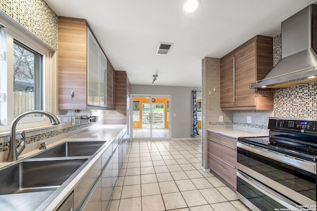 kitchen featuring light tile patterned floors, visible vents, range with two ovens, wall chimney exhaust hood, and a sink