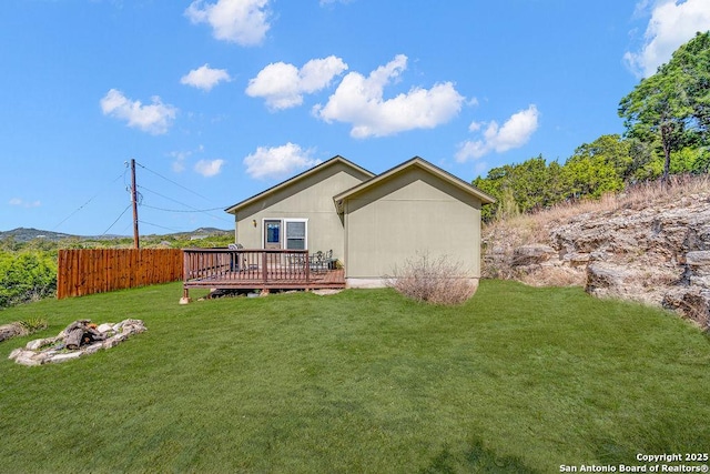 rear view of property with a yard, an outdoor fire pit, fence, and a wooden deck