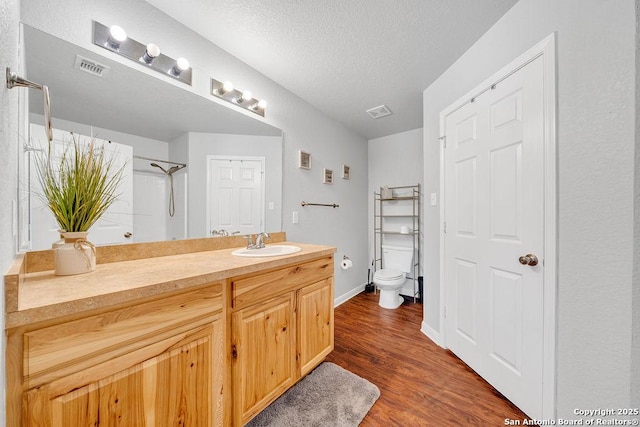 full bath featuring visible vents, toilet, a textured ceiling, vanity, and wood finished floors