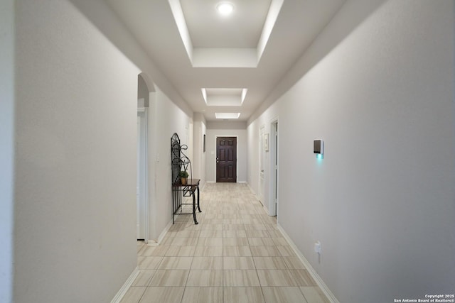 hallway with a tray ceiling, arched walkways, and baseboards