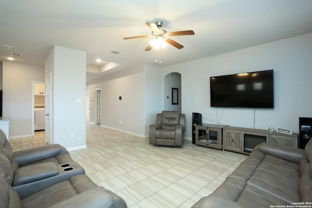 living area featuring arched walkways, light tile patterned flooring, a ceiling fan, visible vents, and baseboards