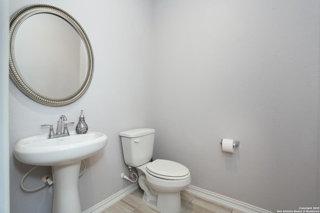 half bathroom with baseboards, a sink, and toilet