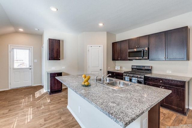 kitchen featuring light wood finished floors, appliances with stainless steel finishes, dark brown cabinets, a sink, and recessed lighting