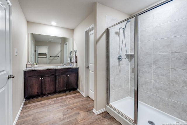 full bath featuring wood finished floors, a shower stall, vanity, and baseboards