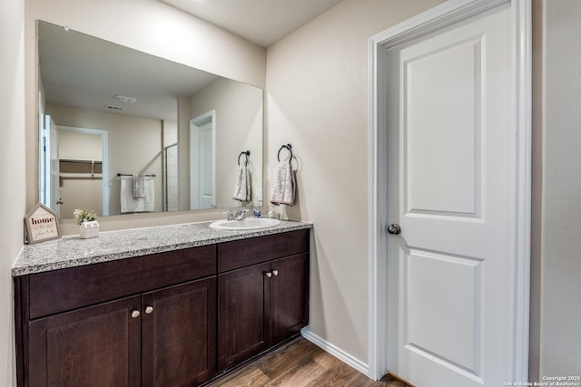 bathroom featuring a shower with shower door, wood finished floors, vanity, and baseboards