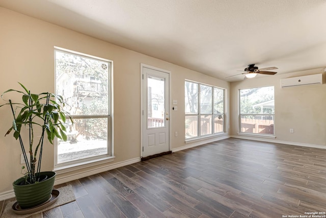 interior space with a ceiling fan, a wall unit AC, dark wood finished floors, and baseboards