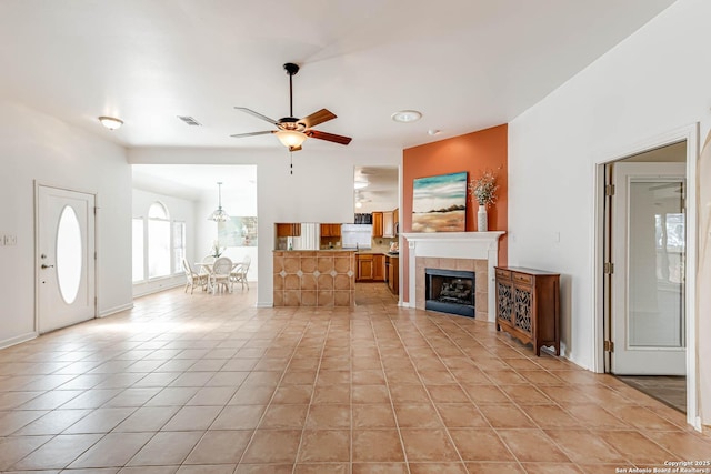 living area featuring light tile patterned floors, a ceiling fan, visible vents, and a tiled fireplace