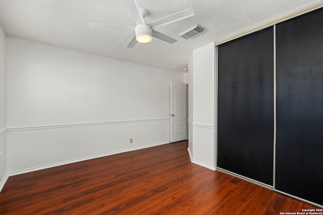 unfurnished bedroom featuring a closet, visible vents, a ceiling fan, a textured ceiling, and wood finished floors