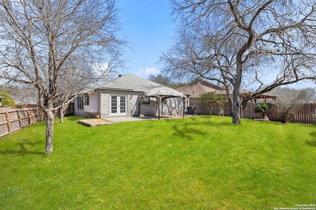 back of house featuring french doors, brick siding, a lawn, a gazebo, and a fenced backyard