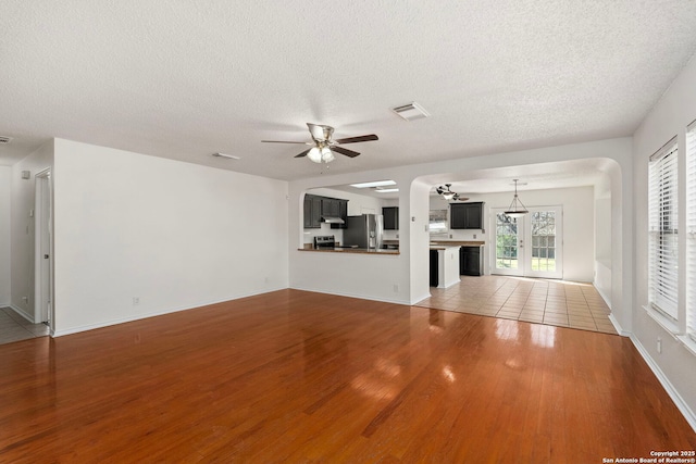 unfurnished living room with light wood finished floors, a textured ceiling, visible vents, and a ceiling fan