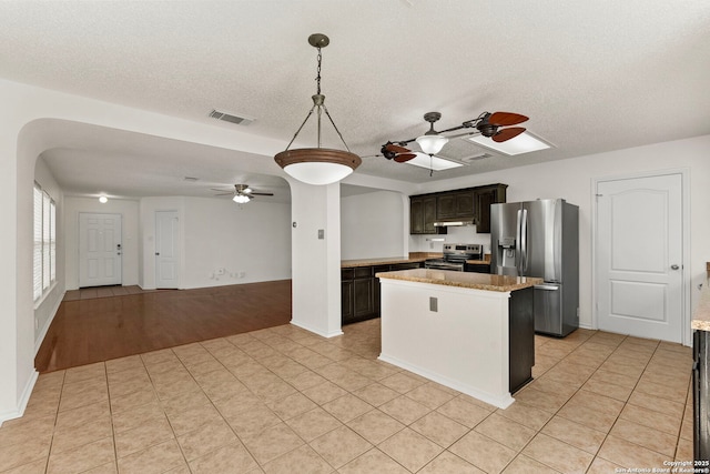 kitchen featuring arched walkways, a kitchen island, visible vents, a ceiling fan, and appliances with stainless steel finishes