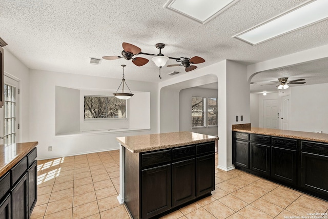 kitchen featuring visible vents, a kitchen island, dark cabinets, light countertops, and light tile patterned flooring