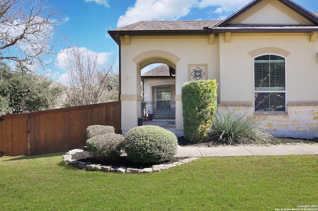 view of front of property with a shingled roof, a front yard, fence, and stucco siding