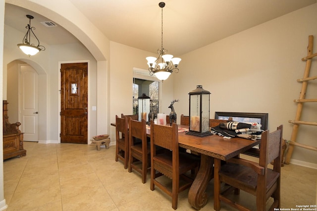 dining area with light tile patterned floors, visible vents, arched walkways, baseboards, and a chandelier