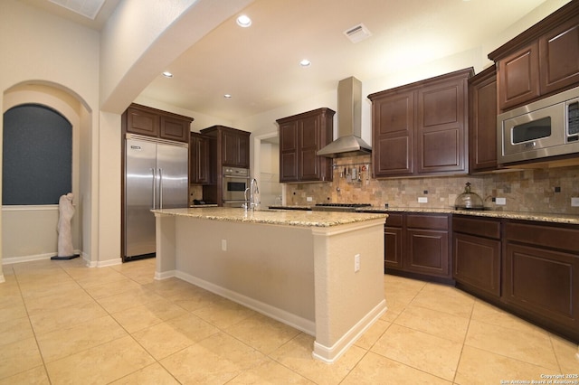 kitchen with visible vents, arched walkways, decorative backsplash, wall chimney exhaust hood, and appliances with stainless steel finishes