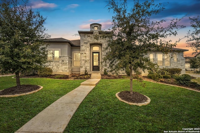 view of front of house with stone siding, a yard, and stucco siding