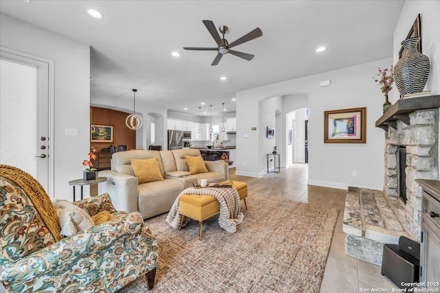 living area with baseboards, arched walkways, a ceiling fan, a stone fireplace, and recessed lighting