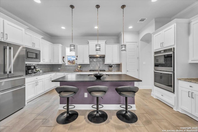 kitchen featuring visible vents, appliances with stainless steel finishes, crown molding, under cabinet range hood, and a kitchen bar