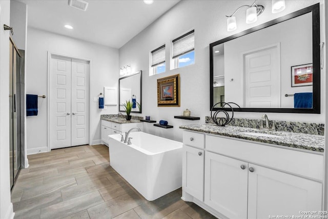 full bath with a sink, wood tiled floor, a freestanding tub, two vanities, and recessed lighting