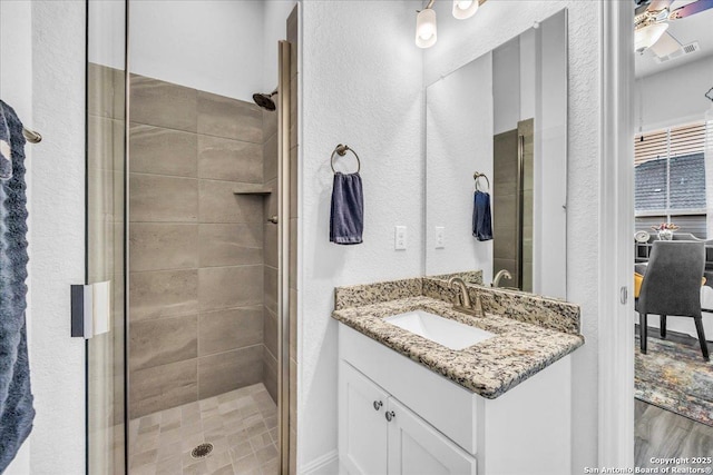 full bathroom with a textured wall, a shower stall, and vanity