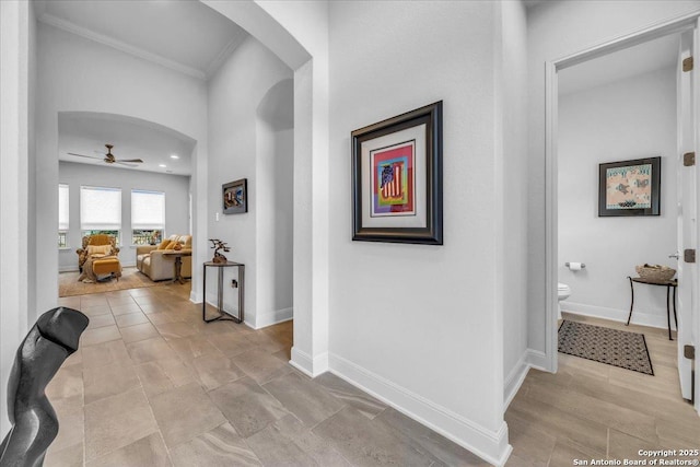 corridor featuring arched walkways, crown molding, and baseboards