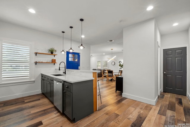 kitchen featuring hardwood / wood-style flooring, a peninsula, stainless steel dishwasher, a kitchen bar, and a sink