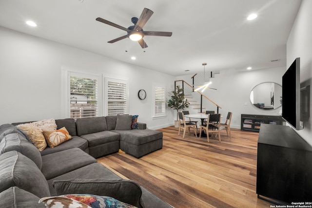 living room with light wood-style floors, baseboards, ceiling fan with notable chandelier, and recessed lighting