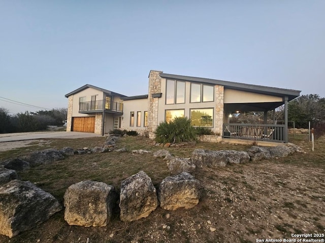 modern home featuring a balcony, stone siding, an attached garage, a porch, and stucco siding