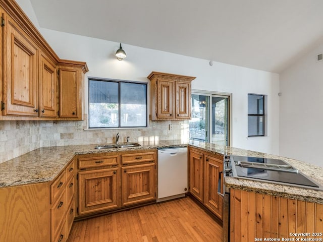 kitchen featuring white dishwasher, a peninsula, stove, vaulted ceiling, and light wood finished floors