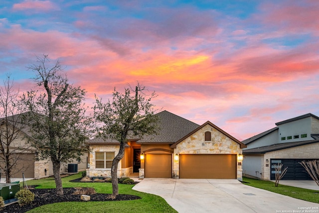 view of front of property featuring a garage, driveway, a lawn, stone siding, and central AC