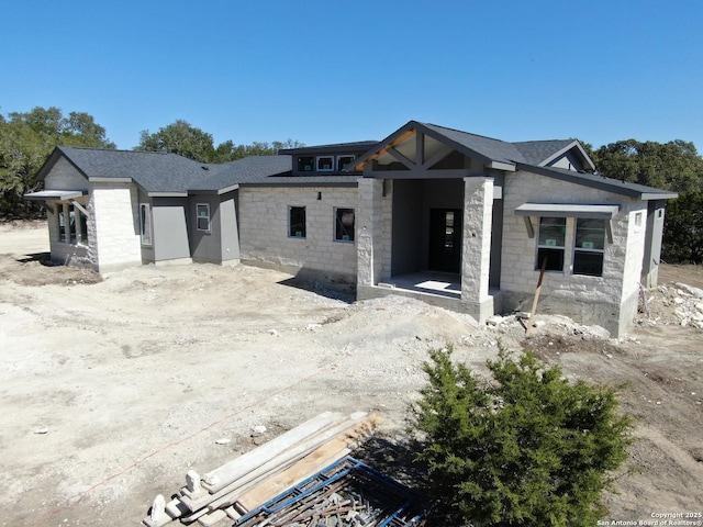 view of front of home featuring stone siding and roof with shingles