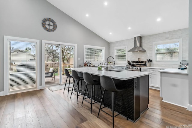 kitchen with wall chimney exhaust hood, stainless steel range with gas stovetop, a sink, light wood-type flooring, and a kitchen bar