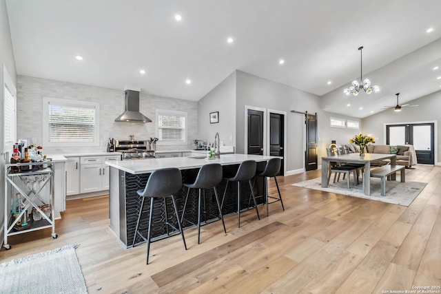 kitchen featuring a barn door, stainless steel range, light countertops, light wood-type flooring, and wall chimney range hood