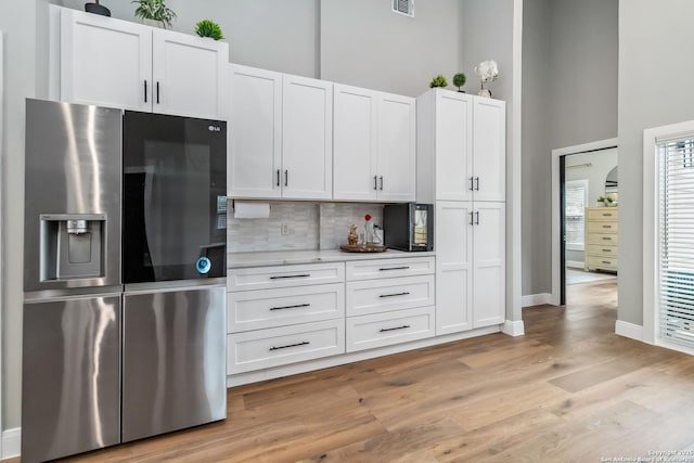 kitchen featuring light wood-style flooring, white cabinetry, stainless steel refrigerator with ice dispenser, and a high ceiling