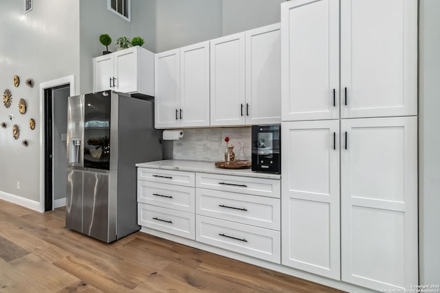 kitchen featuring visible vents, white cabinetry, light wood-style floors, tasteful backsplash, and stainless steel fridge