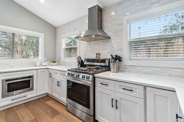 kitchen with wood finished floors, oven, range hood, vaulted ceiling, and gas stove