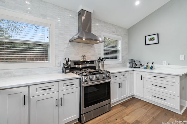 kitchen with light wood finished floors, tasteful backsplash, lofted ceiling, wall chimney exhaust hood, and gas stove