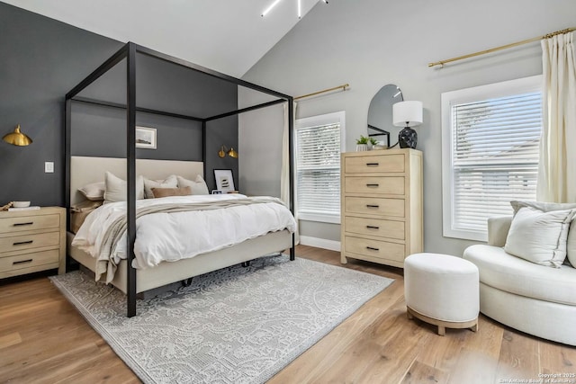 bedroom with high vaulted ceiling, baseboards, and wood finished floors