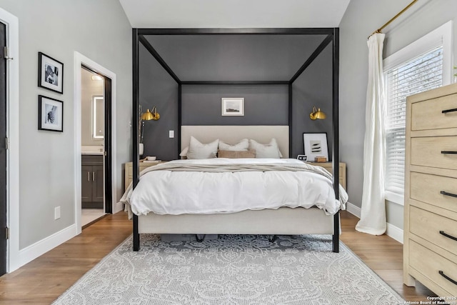 bedroom with ensuite bath, baseboards, and wood finished floors