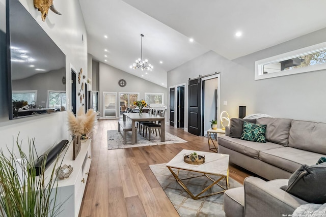 living area featuring high vaulted ceiling, a barn door, recessed lighting, wood finished floors, and an inviting chandelier