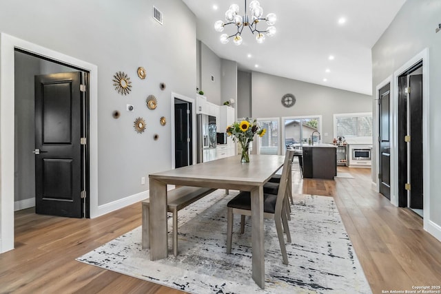 dining room featuring high vaulted ceiling, light wood-style flooring, a chandelier, and baseboards