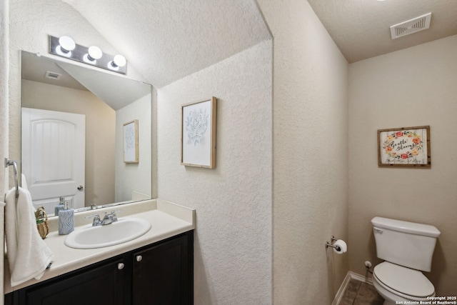 bathroom featuring toilet, a textured wall, visible vents, and vanity