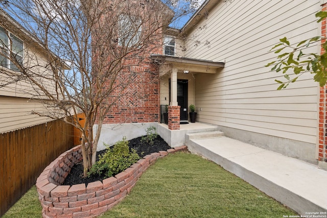 property entrance featuring fence, a lawn, and brick siding