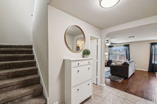 staircase featuring visible vents, a ceiling fan, a textured ceiling, baseboards, and tile patterned floors