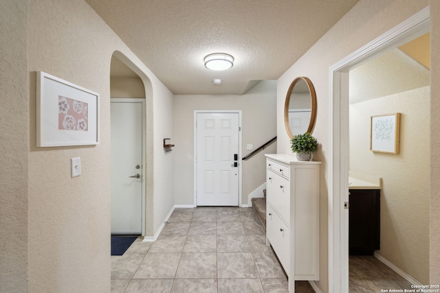 foyer entrance featuring stairway, light tile patterned flooring, a textured ceiling, and baseboards