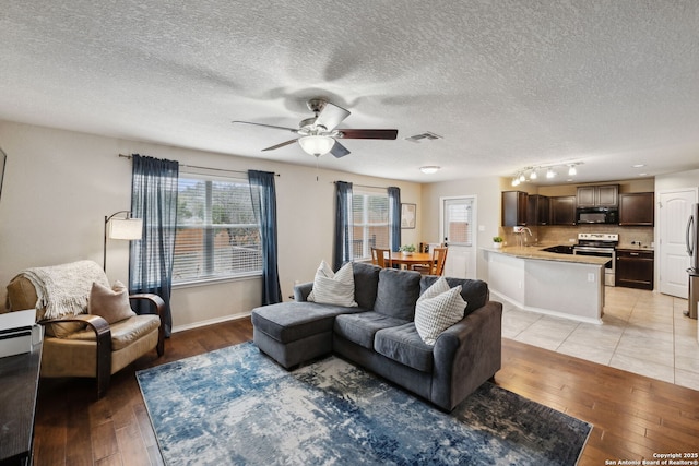 living room with baseboards, visible vents, ceiling fan, a textured ceiling, and light wood-type flooring